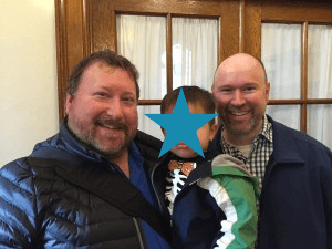 Two proud fathers holding their young child.