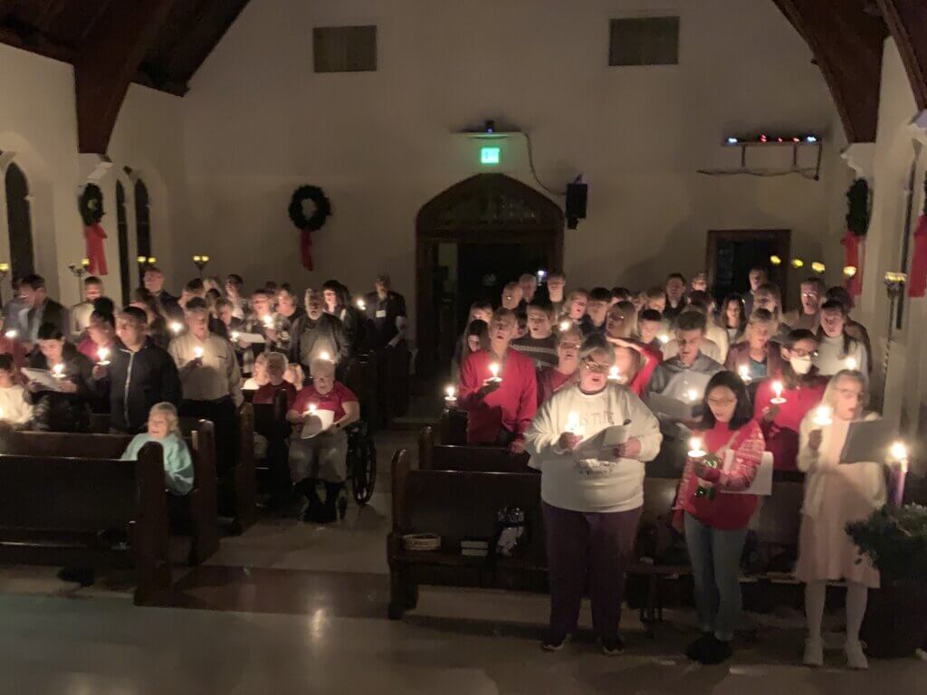 A large group of parishioners holding lit candles in the darkened sanctuary on Christmas Eve.